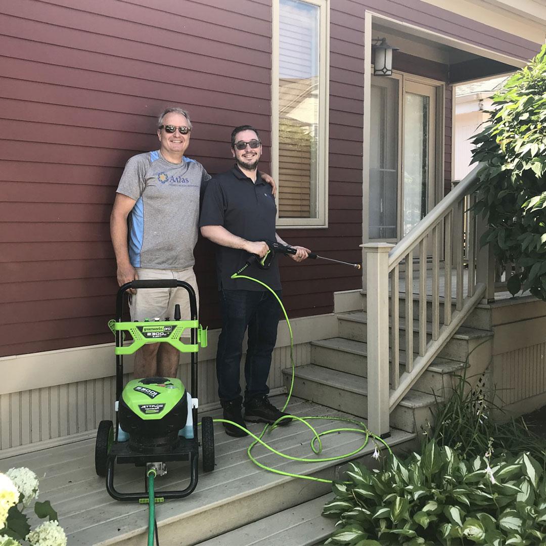 Two volunteers pose near the steps of the Ronald McDonald House with a power washer