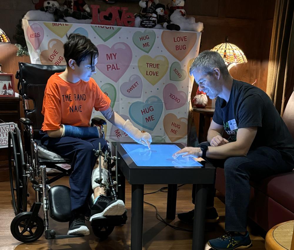 A father and son play a game on an electronic game table in the hospital.