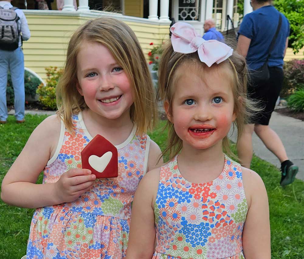 Two young girls smiling with a red cookie shaped like the new Ronald McDonald House logo