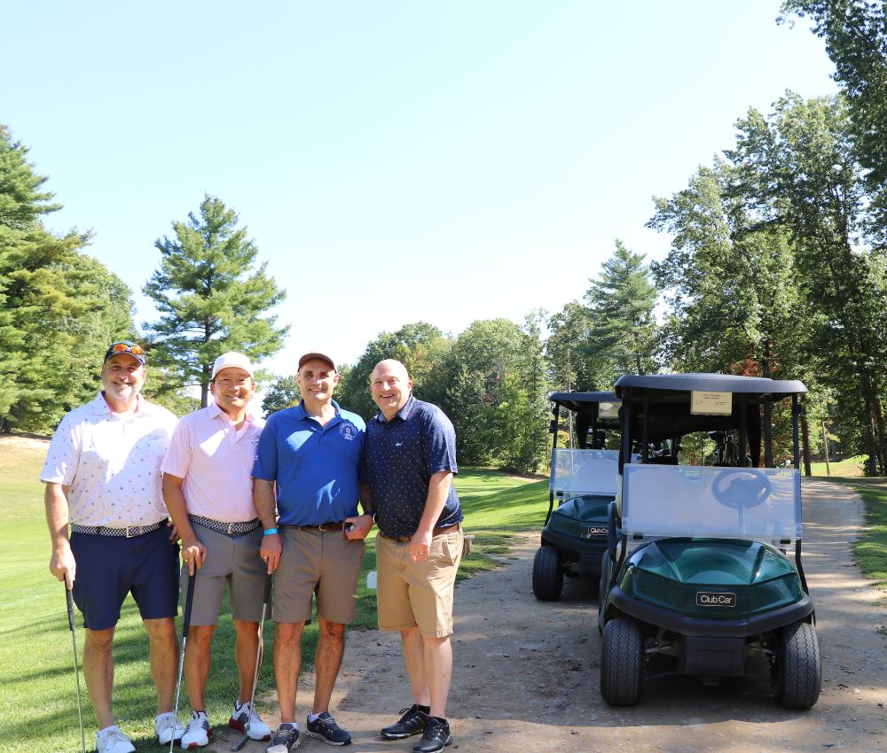 Group of four golfers standing next to golf cart on course