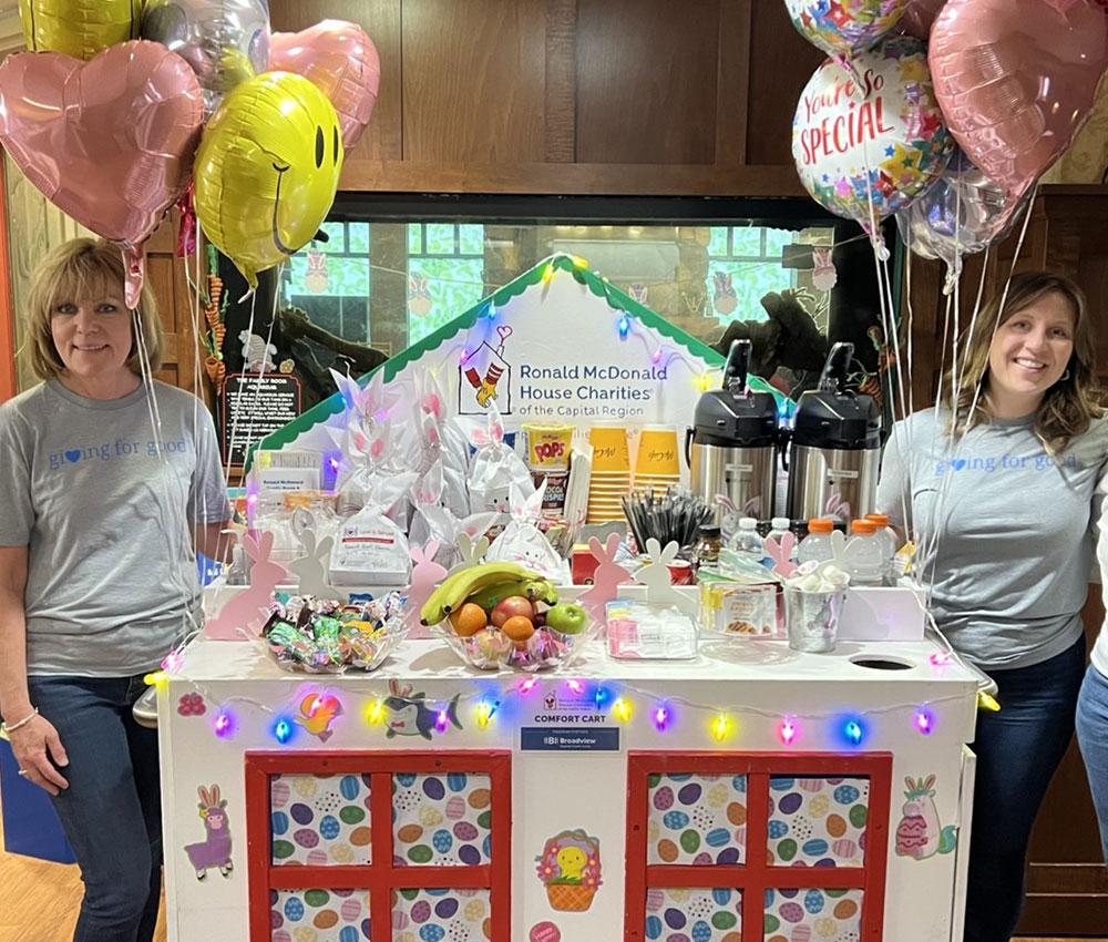 Two women pose around the Comfort Cart in the Ronald McDonald House Family Room at Albany Medical Center