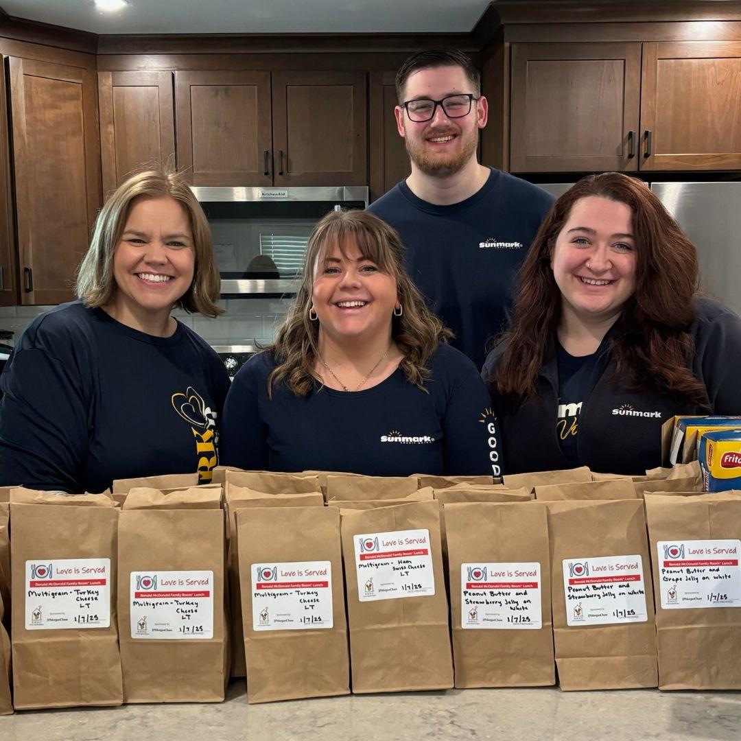 Volunteers pose in a kitchen with an assortment of bagged lunches they've prepared