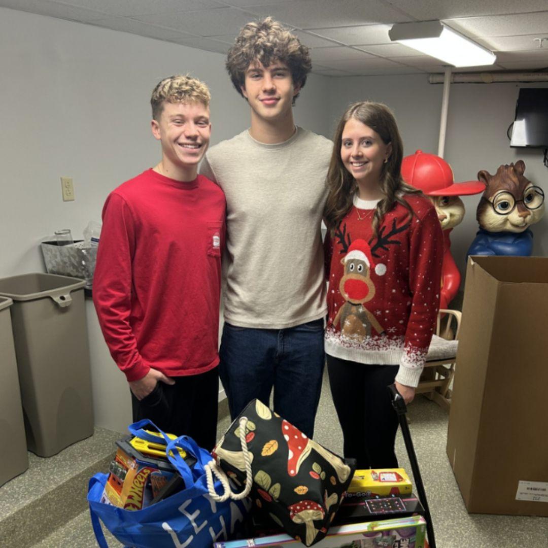 Three teens pose with a wagon of supplies they are sorting at the Ronald McDonald House