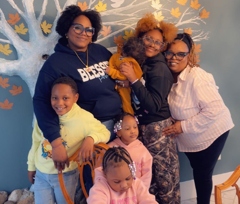 A family of seven hugs and smiles in front of a decorative wall in the Ronald McDonald House Family Retreat at Krantz Cottage.